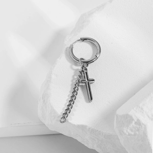 Polished stainless steel cross chain earrings displayed on white textured stone decor
