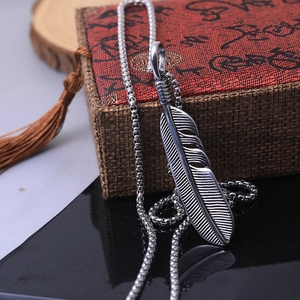Vintage stainless steel feather pendant necklace with box chain on a rustic gift box