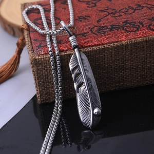 Vintage stainless steel feather pendant necklace displayed on a woven texture gift box