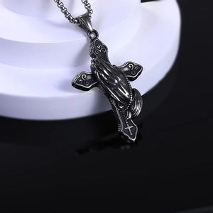 Gros plan du pendentif croix et mains en prière en acier inoxydable vieilli