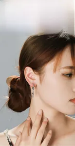 Close-up of a silver stainless steel hoop earring with a cross pendant on a model