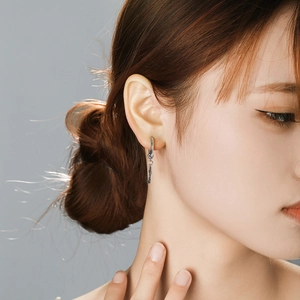 Minimalist silver cross pendant earring in stainless steel worn by a model in profile