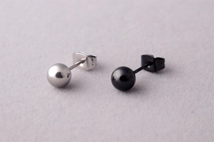 Close-up of minimalist silver and black ball stud earrings on purple textured fabric