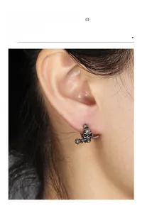 Close-up of gothic skull earring with rose in mouth on model's ear, dark silver finish