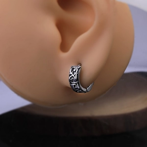 Macro detail of vintage stainless steel hoop earring with engraved dragon patterns