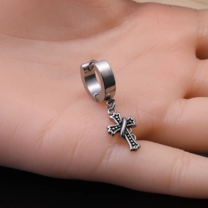 Detail of a vintage punk cross pendant earring in silver alloy on a hand model background