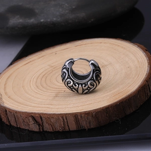 Detailed view of vintage tribal pattern earrings on wood and pebble background