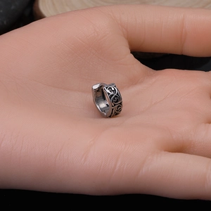 Detailed close-up of retro silver stainless steel hoop earring with tribal dragon engraving