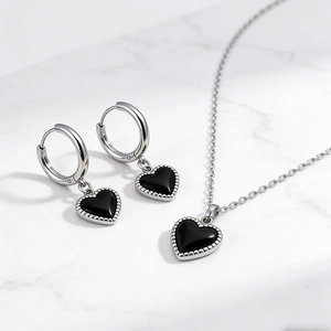 Detail van zilveren oorbellen en ketting met zwarte hart hanger op wit marmer