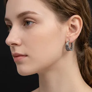 Modern multilayer silver hoop earrings with textured ribbed design worn by a model
