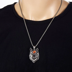 Gros plan du pendentif tête de loup vintage argenté avec perle orange sur un homme