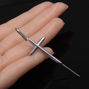 Gros plan d'une boucle d'oreille croix en acier inoxydable argenté poli sur main