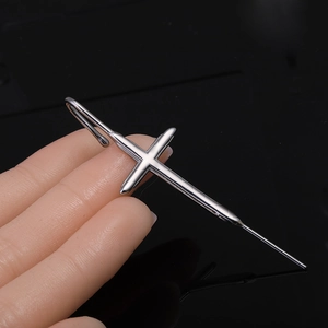 Vue rapprochée d'un pendentif en forme de croix en argent poli tenu à la main