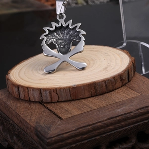 Détail d'un pendentif crâne de dinosaure en acier 316L avec os sur socle en bois