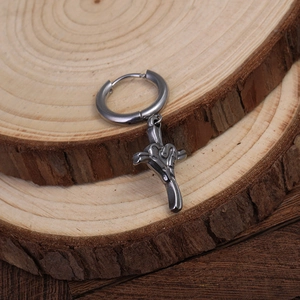 Macro shot of retro stainless steel cross pendant earring on natural wood background