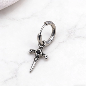 Detail of vintage gothic cross earring with black zircon inlay on a marble surface