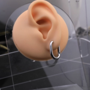 Close-up of silver U-shaped oval hoop earrings on a silicone ear model with high polish