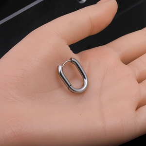 Close-up of a polished silver U-shaped hoop earring held in hand with black background