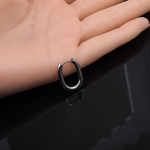 Detail view of gunmetal Mobius twisted oval hoop earring held in hand for scale