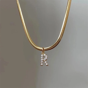 Close-up of golden snake chain necklace with a zircon-encrusted letter R pendant