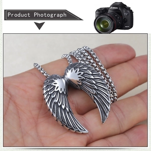 Detailed view of silver angel wing pendant with feather texture held in hand
