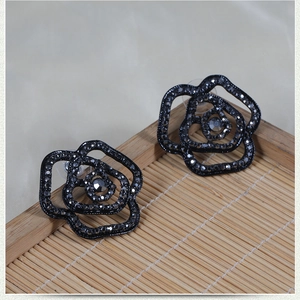 Detail view of black rose stud earrings with full pavé crystals on a wooden tray