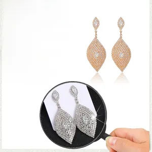 Détail macro de strass étincelants sur de longues boucles d'oreilles feuilles en or et argent