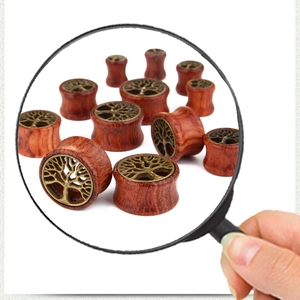 Close-up of wood ear plug with bronze Tree of Life inlay under a magnifying glass