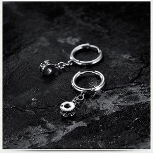 Industrial silver stainless steel hoop earrings with cylinder pendant on rock background