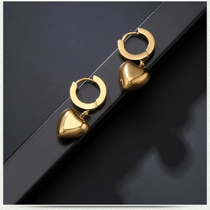Polished gold heart drop earrings on a black display stand with a minimalist punk design
