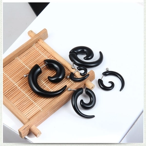 Macro detail of black spiral snail stud earrings set with polished finish on bamboo decor