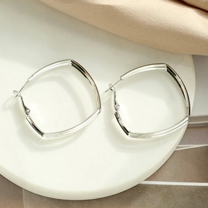 Close-up of silver square hoop earrings on a white plate with elegant soft fabric