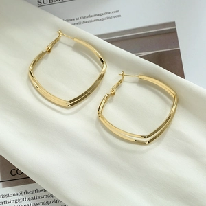 Close-up of geometric gold drop earrings on a minimalist white fabric and magazine background