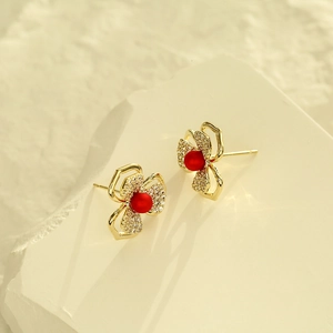 Elegante goldene Blumenohrstecker mit roten Perlen und weißen Steinen auf Steingrund