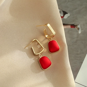 Retro geometric earrings with red matte pendants on elegant champagne satin fabric background