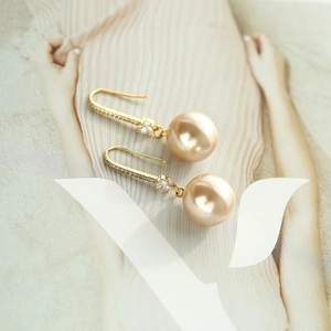 Gros plan de boucles d'oreilles perles champagne et crochets dorés sur un magazine