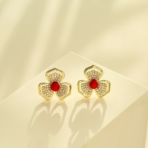 Detail von Gold-Blumenohrringen mit weißen Zirkonia und roten Perlen auf einem Sockel