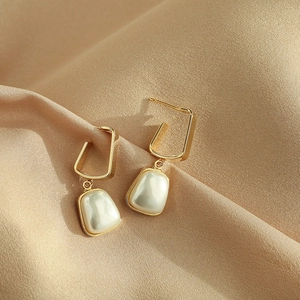Golden geometric U-shaped earrings with white pearls on a soft silk fabric background