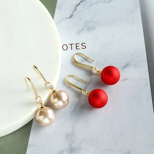 Détails de boucles d'oreilles pompons rouges et perles champagne avec strass sur marbre
