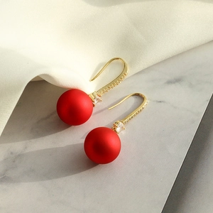 Gros plan de boucles d'oreilles boules rouges mates avec crochets dorés et zircons clairs