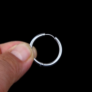 Polished silver stainless steel hoop earring held between fingers on black background
