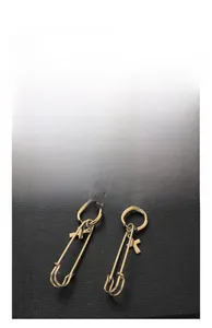 Detailed view of gold safety pin earrings featuring a minimalist cross charm pendant