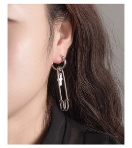 Close-up of punk style silver stainless steel hoop earring with safety pin and cross pendant