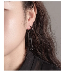 Detail of black punk safety pin earring with a cross charm on male model's ear