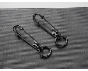 Detail of black safety pin earrings featuring small cross and ring charms in punk style