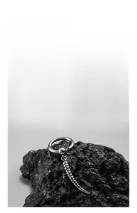 Detailed macro view of silver stainless steel cross earring on dark volcanic rock background