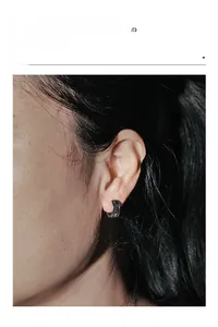 Macro shot of silver stainless steel huggie earring with black star pattern on model