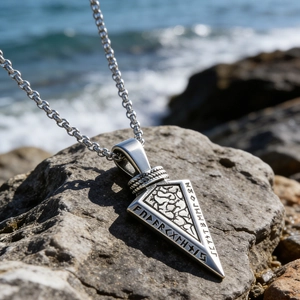 Close-up of Nordic Viking rune arrowhead pendant on a rocky seaside background