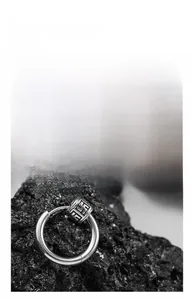 Macro shot of silver stainless steel hoop earring with engraved pattern bead on lava stone