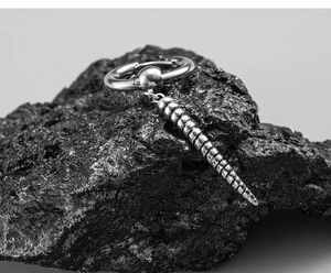 Macro shot of silver stainless steel earring with spiral cone pendant on dark rock